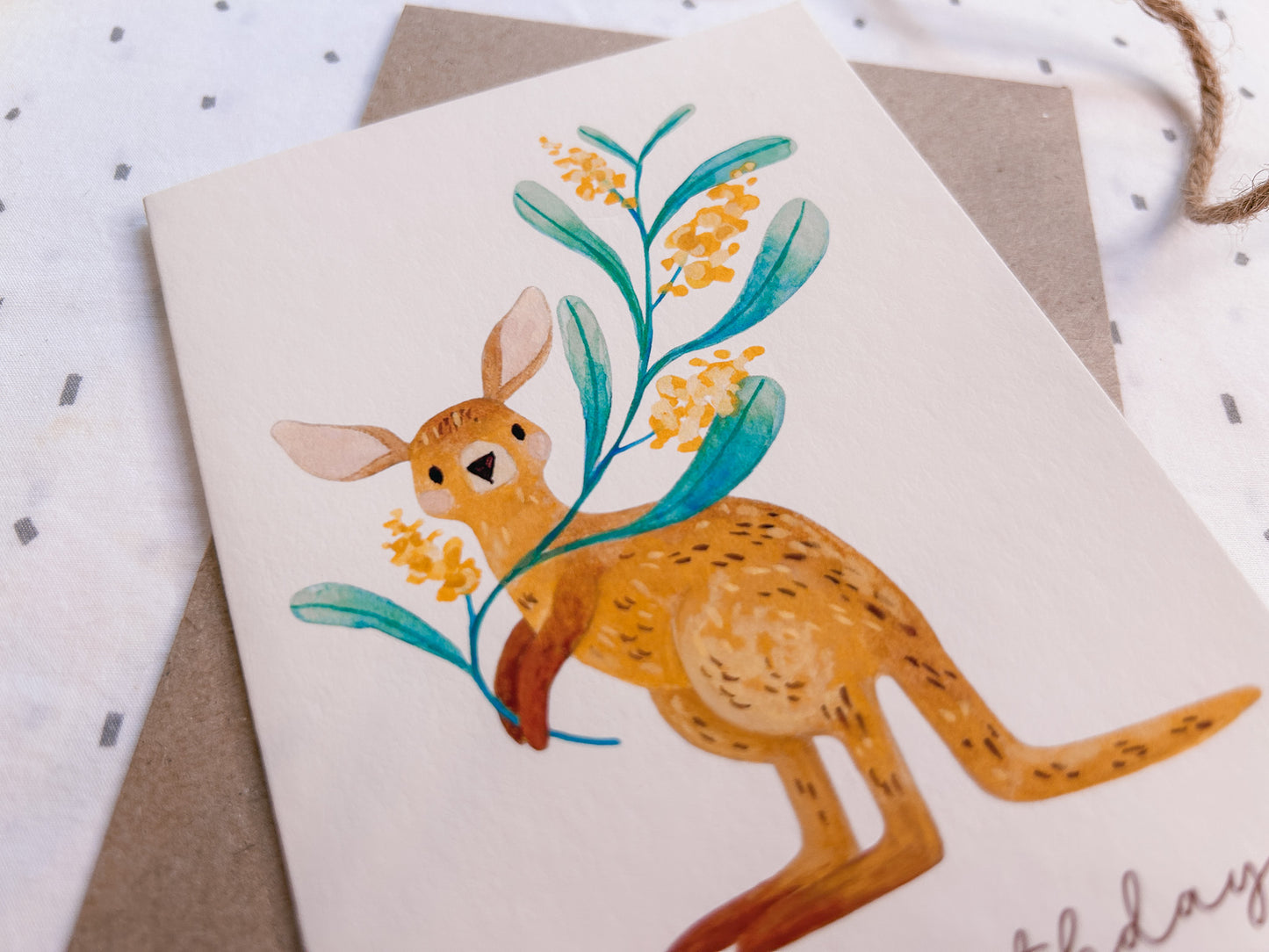 Front close up of Illustrated kangaroo greeting card holding a wattle branch, hand-drawn Australian wildlife stationery